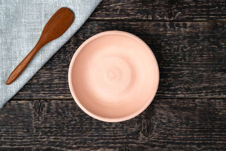 An empty white clay bowl and a wooden spoon on a gray cloth napkin on an old wooden table surface. Copy spaceの写真素材