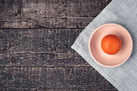 Tangerine in a white clay bowl on a gray cloth napkin on an old wooden table surface. Flat layの写真素材
