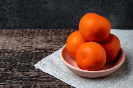Tangerines in a white clay bowl on a gray cloth napkin on an old wooden table surface. Flat layの写真素材