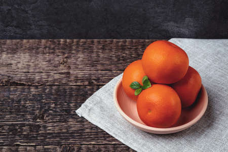 Tangerines in a white clay bowl on a gray cloth napkin on an old wooden table surface. Flat layの写真素材