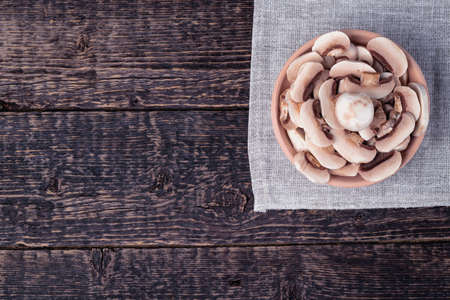 A clay bowl with sliced champignons on a gray napkin against the background of the texture of an old wood. Flat layの写真素材