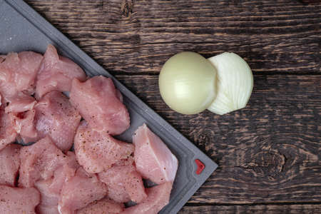 Meat cut into pieces and two halves of an onion on an old textured wooden surface. Flat layの写真素材