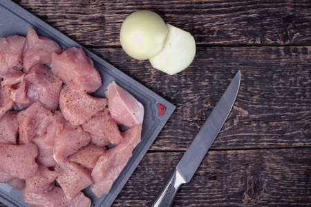 Meat cut into pieces, a knife and two halves of an onion on an old textured wooden surface. Flat layの写真素材