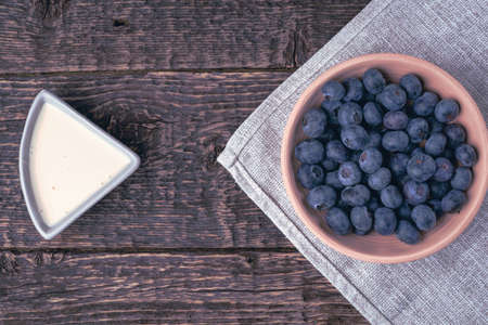 A bowl with blueberries on a gray cloth napkin and yogurt on a background of an old wooden surface.の写真素材