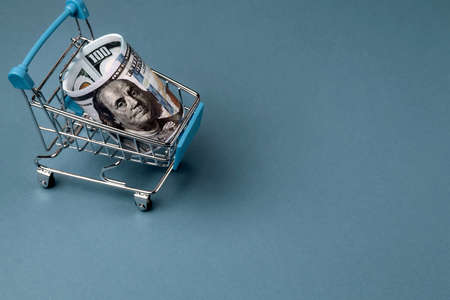 One hundred dollar bills in a shopping trolley on a blue background. Close-up, copy space