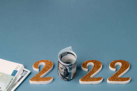 Number 2022 with a roll of one hundred dollar bills and stacks and bundles of money on a blue background. Copy spaceの写真素材