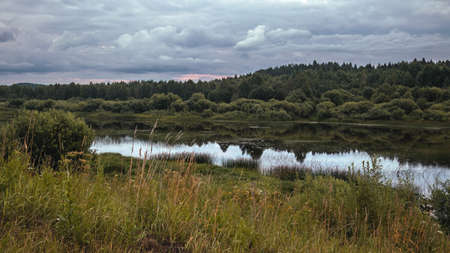 Calm evening view of the river with tree-covered banks and overcast sky reflection. travel conceptの写真素材