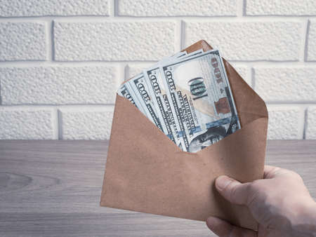 The hand holds a paper envelope with dollar bills. Bonus, reward, benefits conceptの写真素材