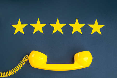 Five star rating and yellow retro phone on a blue background. customer service quality control.の写真素材