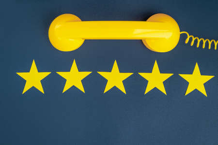 Five star rating and yellow retro phone on a blue background. customer service quality control.の写真素材