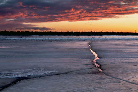 A beautiful dramatic sunset over a frozen river with cracked ice.の写真素材