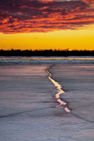 Beautiful sunset over a frozen river with ice cracks. vertical positionの写真素材