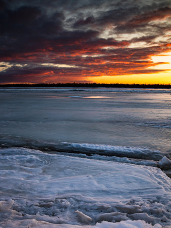 Beautiful sunset over a frozen river with ice cracks. vertical positionの写真素材