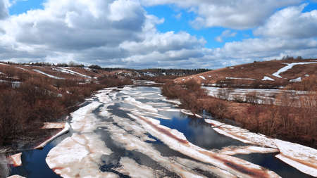 Melting ice on a river in a hilly area under a blue sky with clouds. spring landscapeの写真素材