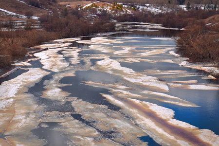 Melting ice on a river in a hilly area with trees. spring landscapeの写真素材