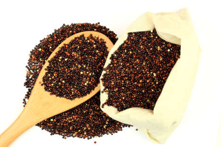 Picture of spilled from white fabric sack (bag) and over wooden spoon edible seeds of Black  Organic Quinoa on white background. の写真素材