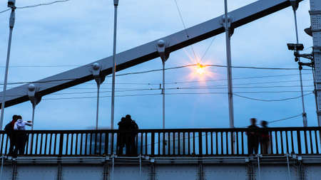silhouettes of young people on steel bridge in dusk 