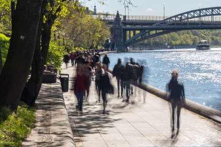 Silhouettes of people walk along the embankment of a city riverの写真素材