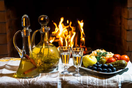 Traditional homemade Russion  herbal infused vodka with cold snacks and firplace on backgroundの写真素材