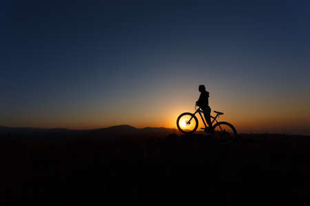 Silhouette of a young female on a mountain bike at sunsetの写真素材