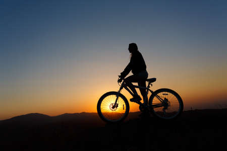 Silhouette of a young female on a mountain bike at sunset