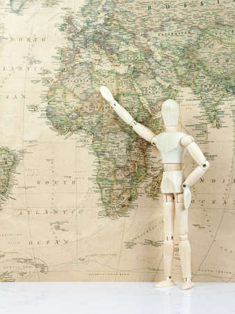 Wooden Mannequin stay with Hand up looking on world map in background