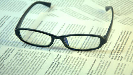 Black-framed glasses lie on the page of the magazine.の写真素材