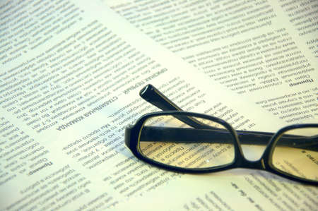 Black-framed glasses lie on the page of the magazine. Close up.