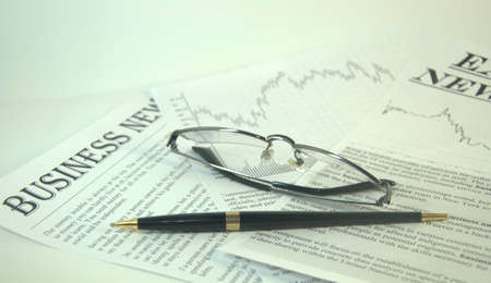 Reading glasses and pen are on the news media. Close up shot.