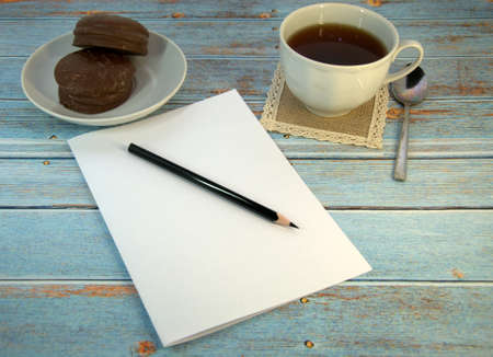 A cup of tea, two chocolate cakes and a sheet of paper with a pencil on a wooden table. Close-up.の写真素材