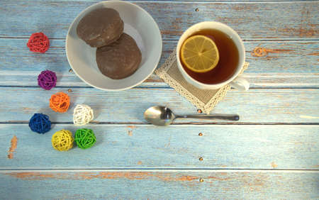 A cup of tea with a slice of lemon, a spoon and a plate of chocolate cake lie on a wooden table with a decoration of colorful balls. Close-up.の写真素材