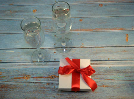 Two glasses with champagne and gift box with satin ribbon on a wooden table. Close-up.の写真素材