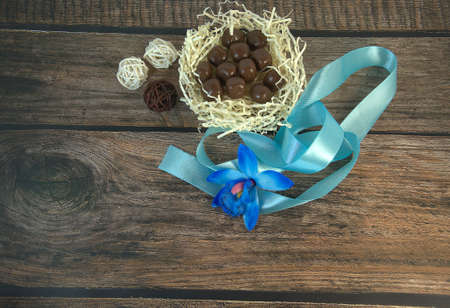 A nest of hay with chocolates, a blue ribbon, a bud of blue orchid and decorative balls on a wooden...