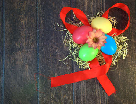 Four painted Easter eggs in a nest of straw with a flower in the center, lying on a scarlet ribbon...