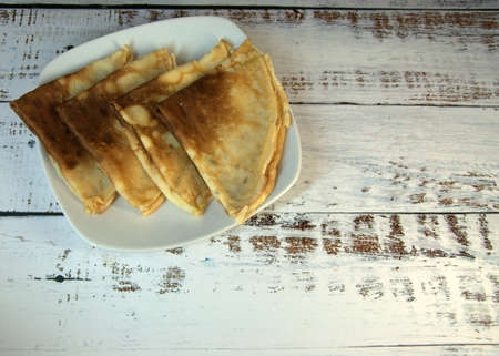 Four fresh pancakes on a ceramic plate lie on a wooden table. Close-up.