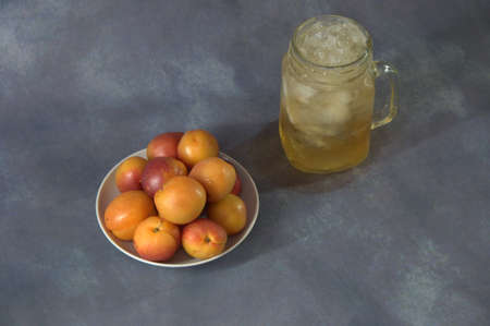 Ripe juicy apricots on a ceramic plate and a mug of apricot juice with ice on a gray abstract...