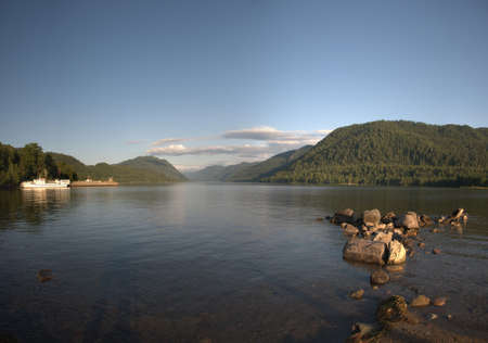 The rocky shore of the lake in the mountains at sunset and the ship at the pier. Teletskoye Lake, Altai, Russia.の写真素材