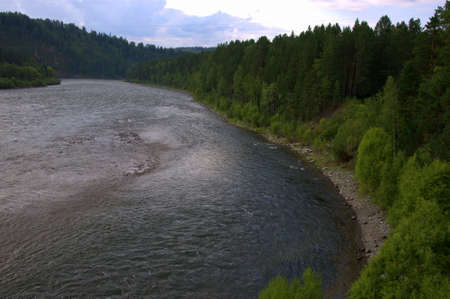 The bend of a calm and wide river flowing through a mountainous wooded valley in the evening. Altai,...