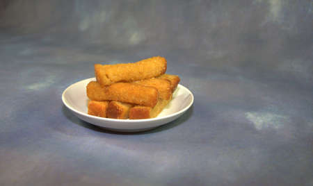 Fresh wheat croutons on a white round plate on a gray abstract background. Close-up.