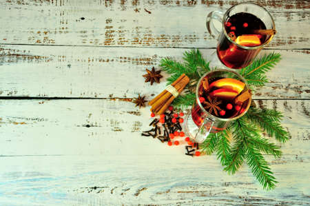 Two glasses with hot wine, slices of fruit and spices, lie on a table surrounded by fir cones and branches. Christmas composition.の写真素材