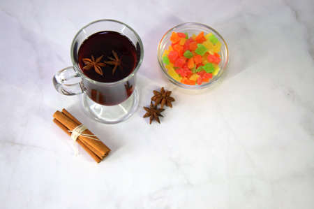 A glass of mulled wine with a slice of orange, anise and a stick of cinnamon is on the table with a...