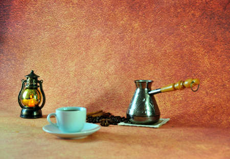 Cezva with coffee on a napkin in a pile of beans, anise and cinnamon, next to a white cup on a...