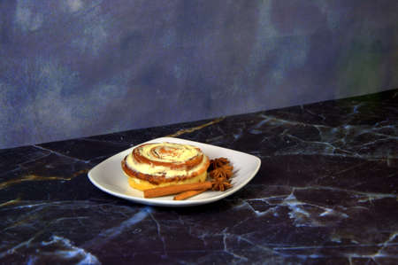 Cinnamon roll in glaze, lies on a white ceramic plate, decorated with anise and cinnamon. Close-up.