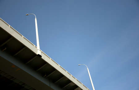 View from below on a part of the bridge with lighting poles and clear blue sky. Close-up.