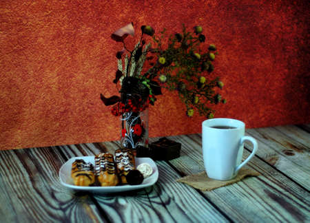 Warm still life, a plate with fresh eclairs, a white ceramic mug with tea on a napkin and a glass...
