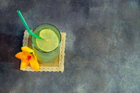 A tall glass of mojito with ice and a straw is standing on a textile napkin next to a vanilla flower on a gray abstract background. Close-up.の写真素材