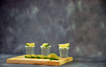 Three glasses of tequila with salt on the edges and lime slices on top, stand on a wooden stand. Close-up.の写真素材