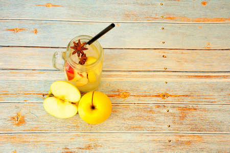 A mug of juice with ice stands on a wooden table, next to two ripe green apples. Close-up.の写真素材
