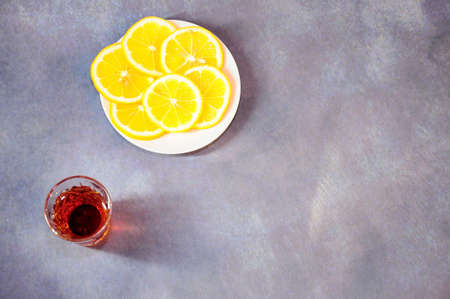 Crystal glass of cognac and a plate with slices of ripe lemon on a gray background. Close-up.