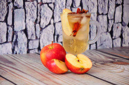 A glass mug of juice with ice and slices of fruit and anise, next to three apple.